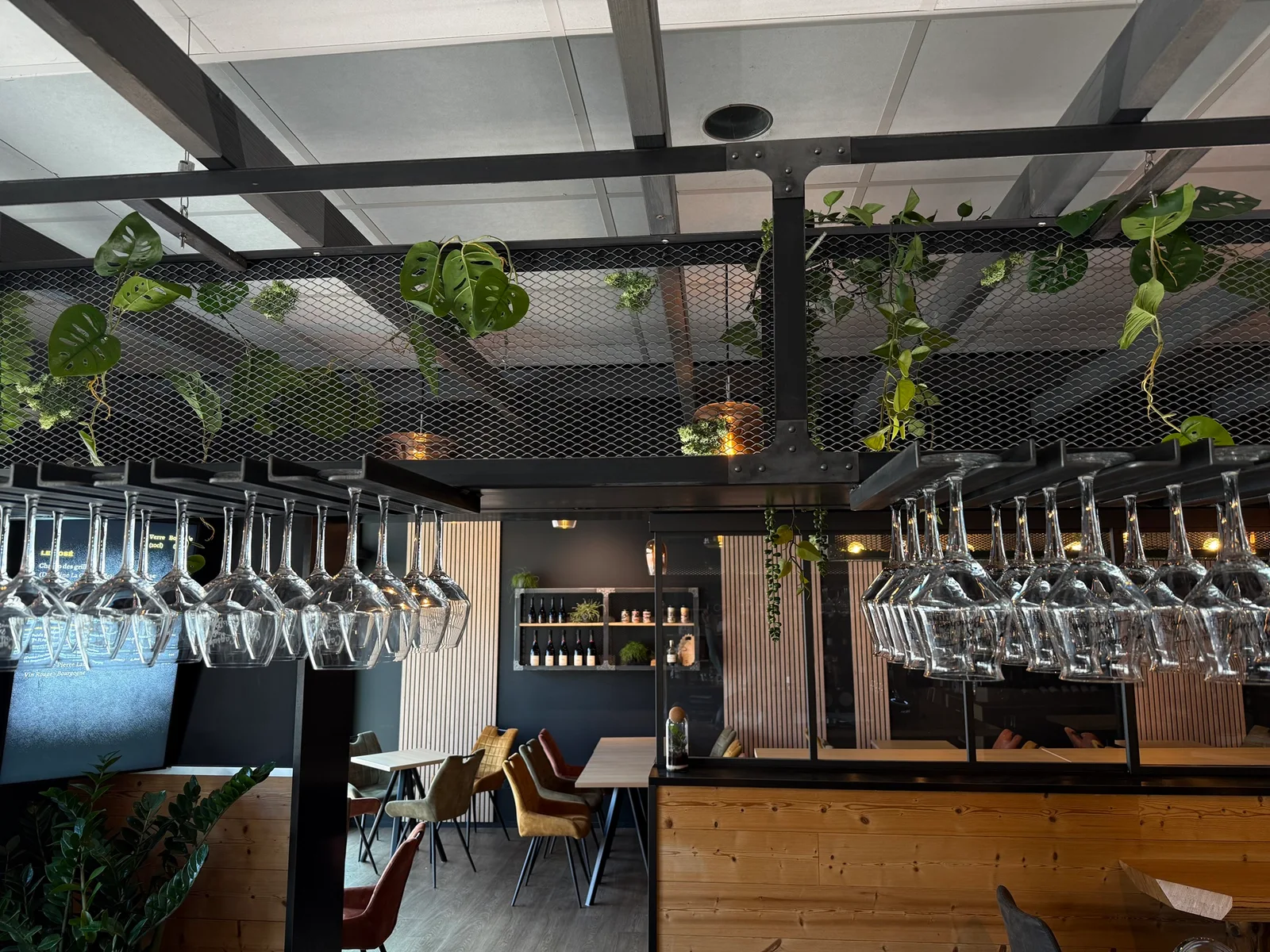 La verrerie suspendue, les plantes et le comptoir en bois du vrai bar Capsule & Bouchon